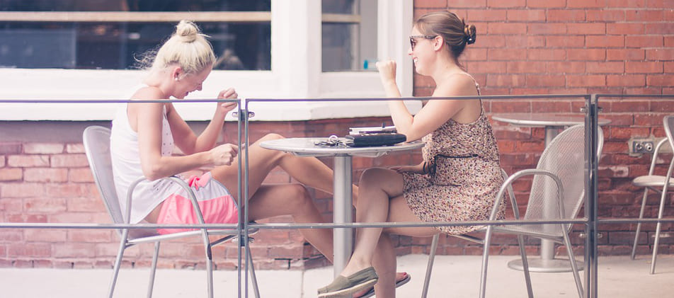 Zwei Freundinnen haben viel Spaß und genießen im Sommer an einem Bistrotisch die neue Schuldenfreiheit durch Hilfe von Schuldnerberater Schuldner-Hotline Bremen Blockland